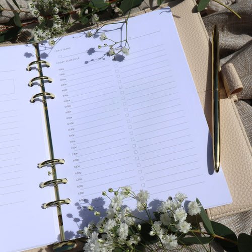 Open planner with a pen and flowers. Planner shows a hourly schedule and task list. 