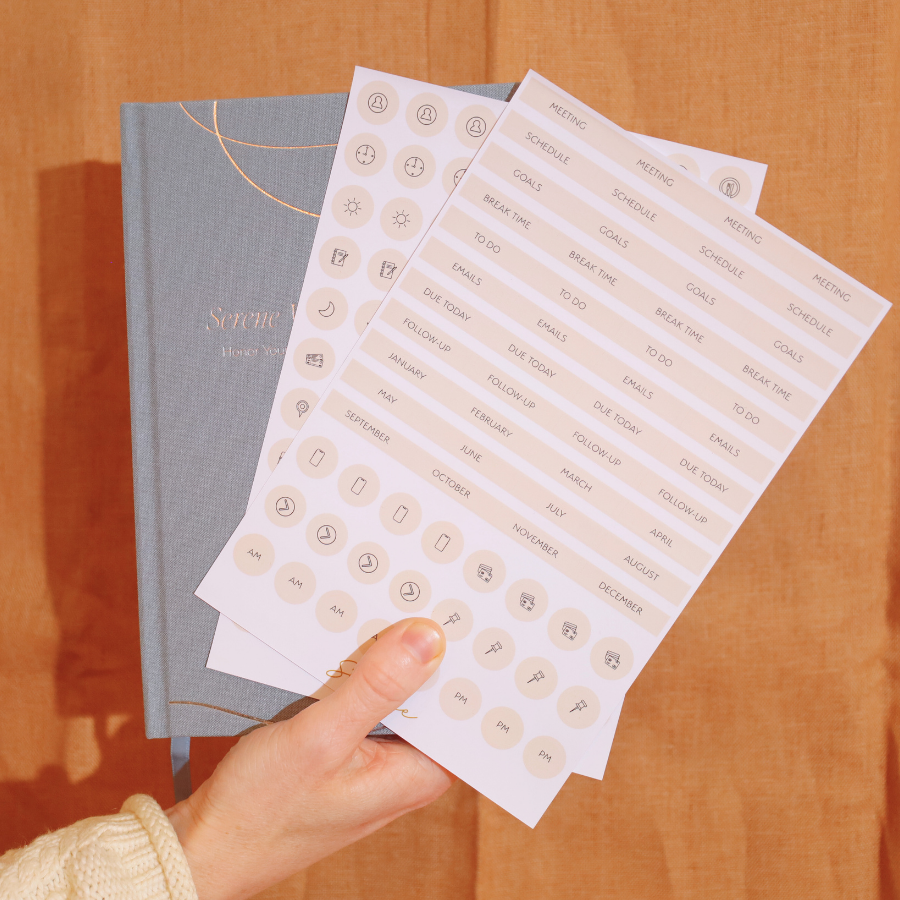 Hand holding a sheet of planner stickers next to a notebook on a wooden surface