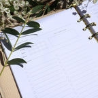 Planner with a self-care plan section on a surface with green leaves and flowers.