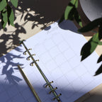 Open planner with monthly layout on a light surface, surrounded by green leaves