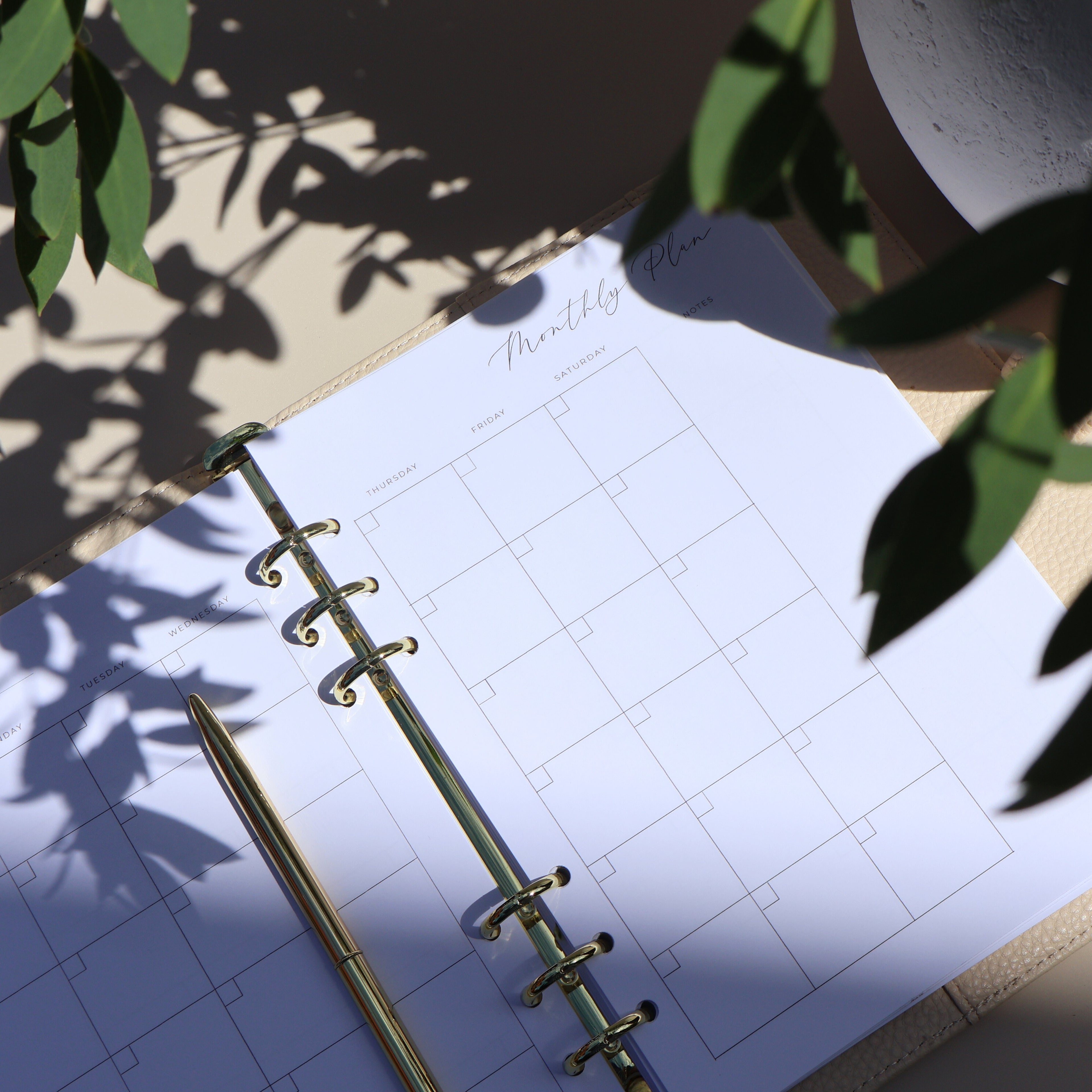 Open planner with monthly layout on a light surface, surrounded by green leaves