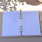 Open planner with blue pages on a light surface, with a pen and decorative item in the background.