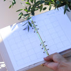 Planner with grid layout held by a hand, with greenery in the background