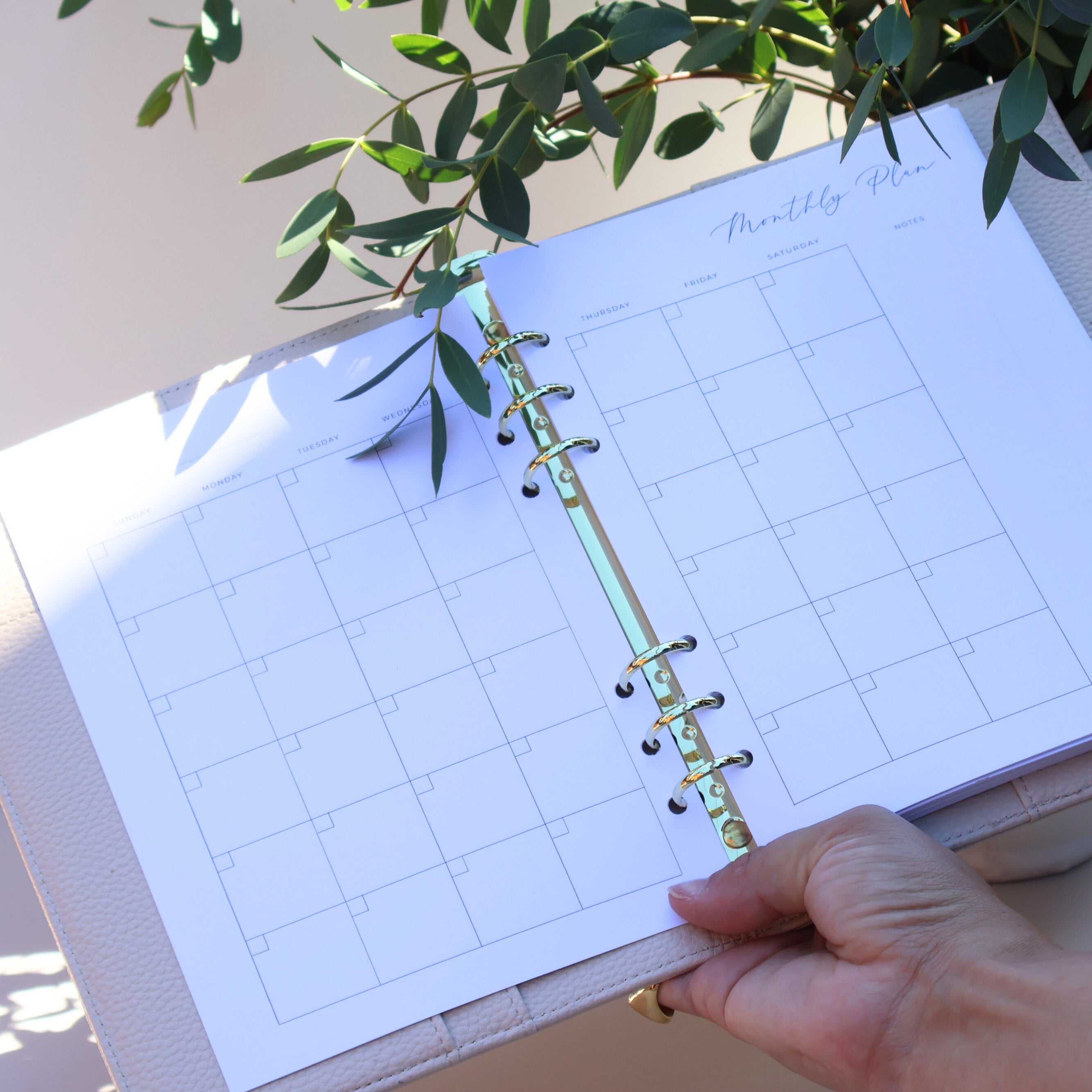 Planner with grid layout held by a hand, with greenery in the background