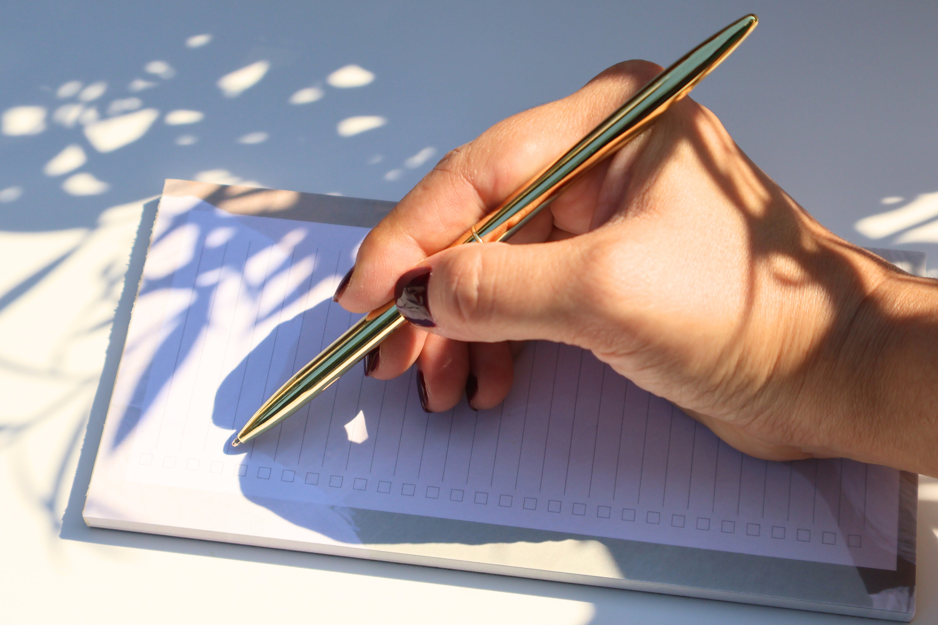 Hand holding a pen over a notebook with a blurred natural background