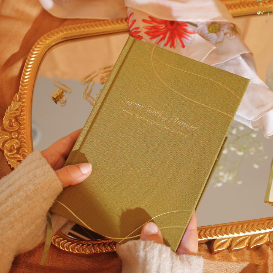 Hand holding a green planner with decorative elements in the background